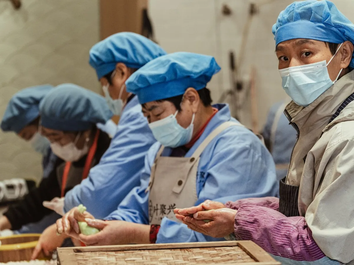 Workers in protective gear and masks preparing food in high-volume industrial central kitchen